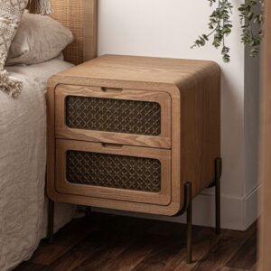 Elegante mesita de noche de Artisa con patas altas de metal y dos cajones en madera. Su frente en metal presenta un diseño geométrico que aporta un toque moderno y sofisticado, ideal para dar carácter a tu dormitorio